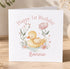 A white greeting card with a cute illustration of a duck surrounded by flowers and plants, along with the text "Happy 1st Birthday Bonnie".