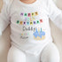 Image showing a baby wearing a white onesie. The onesie is adorned with colorful text that reads: 'HAPPY 30th BIRTHDAY Daddy' and 'Love from Mason,' accompanied by a playful illustration of a blue-iced birthday cake with two lit candles. The background is neutral, bringing focus to the baby's outfit and its celebratory design