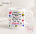 A white ceramic mug with a colorful design featuring text and various illustrations, including hearts, stars, and smiley faces.