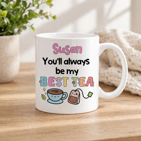A white mug with a colorful design and text that says "You'll always be my best tea" along with illustrations of tea bags and a cup of tea.