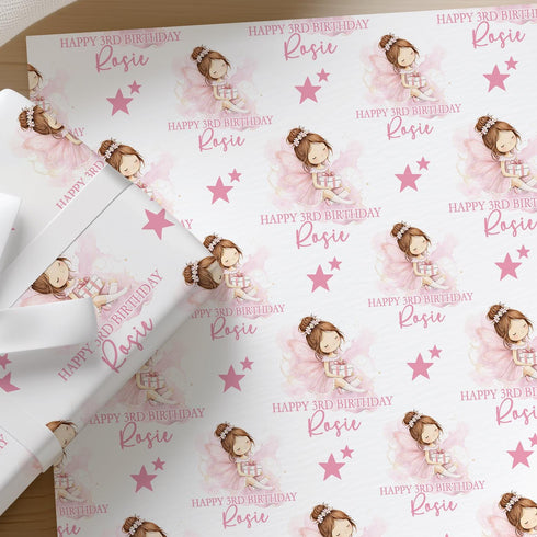 a gift wrapping paper with a repeating pattern of a girl with a bow on her head and stars. The paper has the name "Riley" written on it in pink. The wrapping paper is placed on a wooden surface, and there are some white flowers in the background.