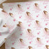 a gift wrapping paper with a repeating pattern of a girl with a bow on her head and stars. The paper has the name "Riley" written on it in pink. The wrapping paper is placed on a wooden surface, and there are some white flowers in the background.