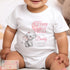 The image depicts a baby dressed in a white onesie with a cute custom design. The design features a baby elephant holding a pink balloon surrounded by hearts. The text says, "Happy FIRST BIRTHDAY as my Daddy love from Charlotte." This thoughtful onesie is from the brand "PRINT4YOU personalised gifts." It seems perfect for celebrating a very special milestone!