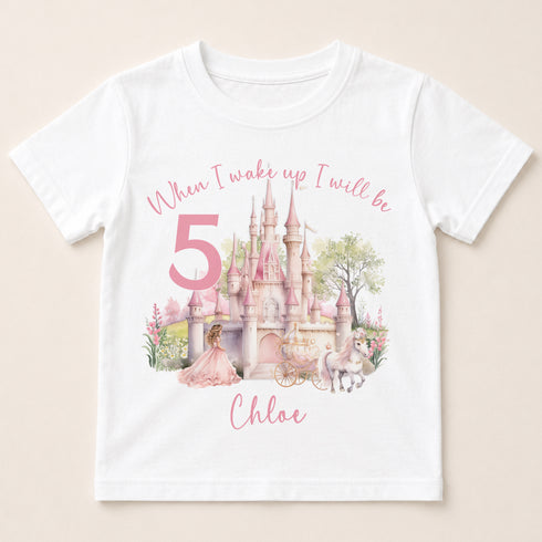 A white t-shirt with a printed design featuring a castle, a princess, and a unicorn, along with the text "When I wake up I will be Chloe" and the number "5".