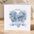 A white card with a heart-shaped arrangement of blue flowers and a blue ribbon banner that says "Mummy".