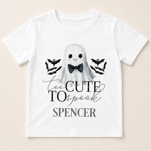 A white t-shirt with a graphic design featuring a ghost character wearing a bow tie, surrounded by bats, and the text "Too Cute to Spook" and "Spenser" below.
