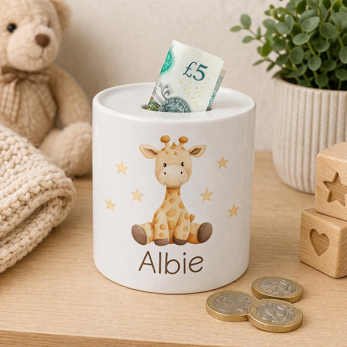 Ceramic giraffe money box with a baby giraffe and gold star illustration, personalised name in brown script, styled with a plush giraffe toy and coins