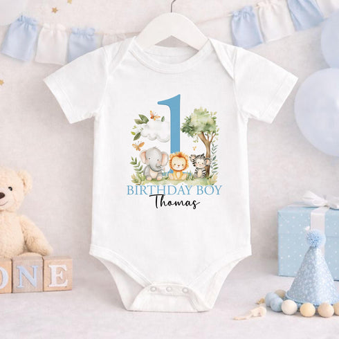Personalised 1st birthday boy outfit with blue number 1, safari animals, elephant, lion, zebra, tree and custom name, shown on bib, vest, sleepsuit, t-shirt and white pyjamas.
