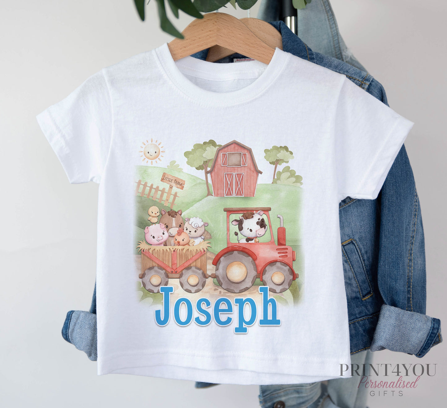 White T-shirt printed with a red tractor, farm animals and a barn, and the personalised name Joseph, displayed on a hanger.