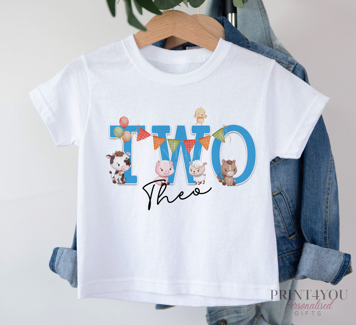 White T-shirt printed with 'TWO' in blue, farmyard animals and the personalised name Theo, displayed on a hanger with a denim jacket.