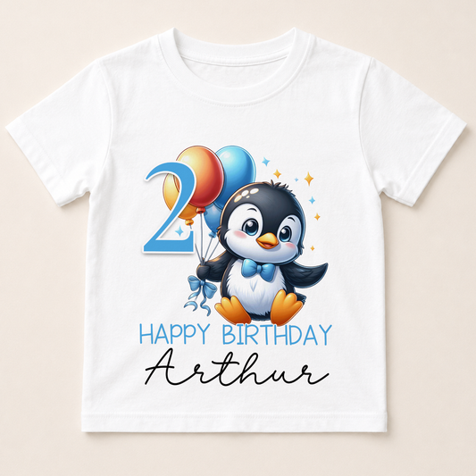 A white t-shirt with a cartoon penguin holding balloons and the number "2" on it, along with the text "Happy Birthday Arthur".