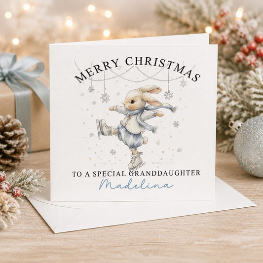 Personalised bunny Christmas card, white 6x6 inch square card printed with a cream bunny in a blue scarf and falling snowflakes with a name