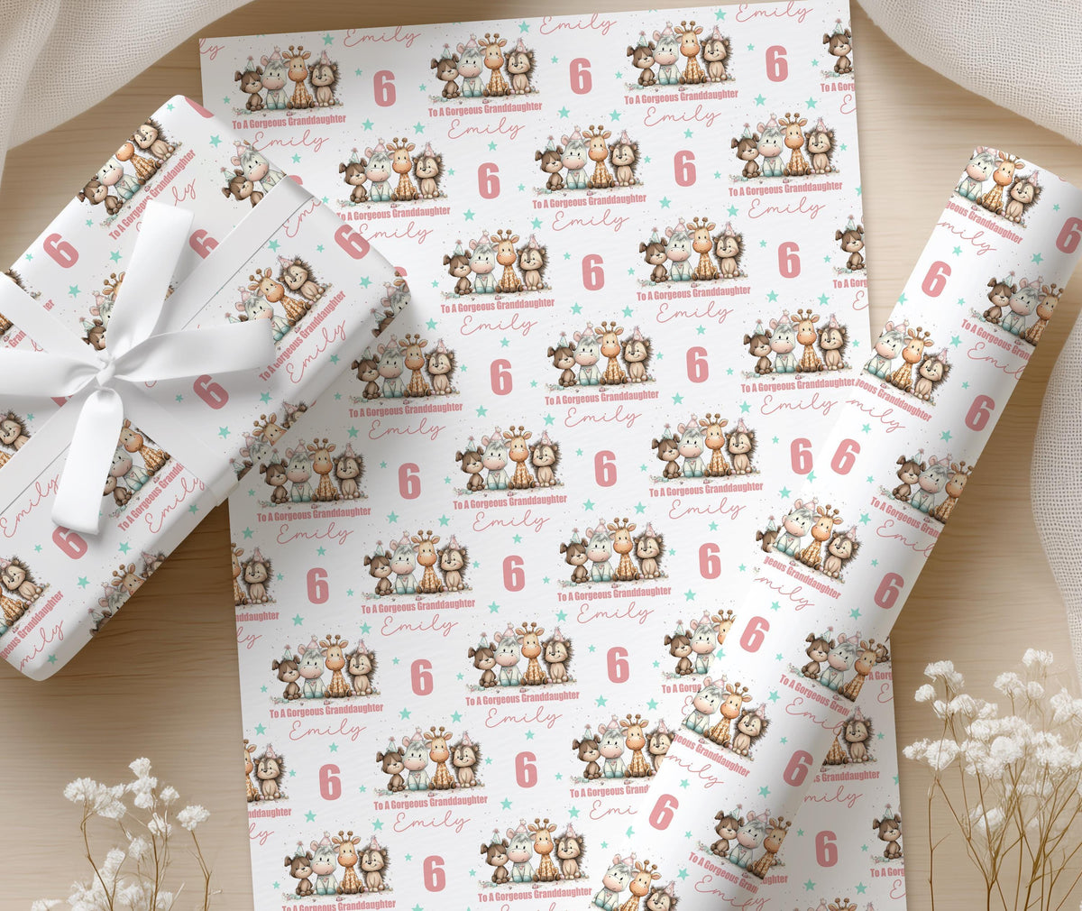 Sheets of personalised wrapping paper printed with elephants and giraffes and the custom name Emilly, displayed on a wooden surface with white flowers