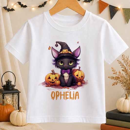 A white t-shirt with a Halloween-themed graphic design featuring a black cat wearing a witch's hat, surrounded by jack-o-lanterns.