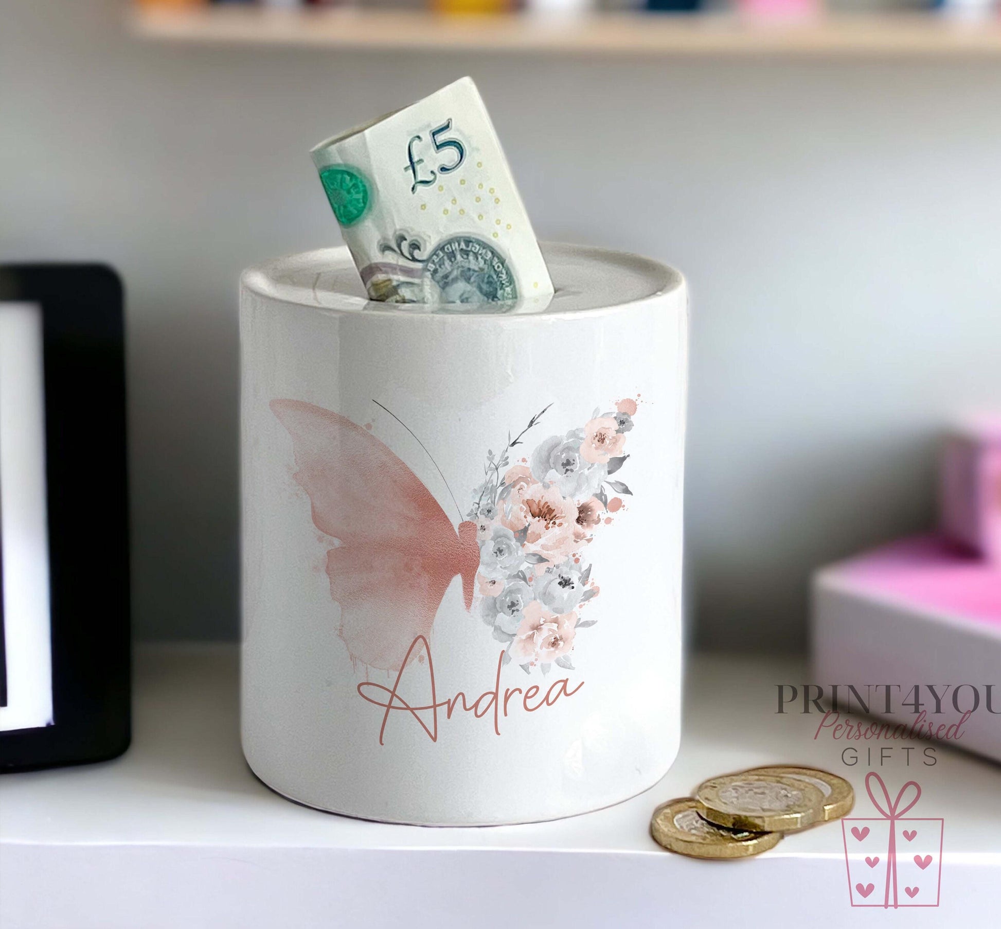 Close-up of the watercolour butterfly and floral design on the personalised ceramic money box, with the name Andrea in pink script