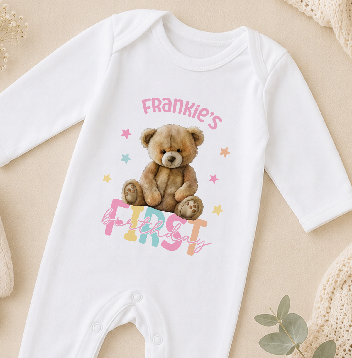 A white onesie with a teddy bear and the text "Frankie's first birthday" printed on it.
