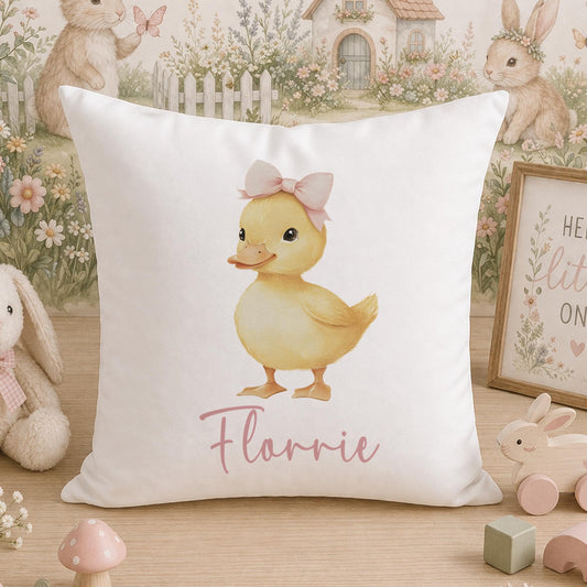 Square white nursery cushion printed with a pink baby duck wearing a bow and personalised with the name Flourrie, styled among soft toys.