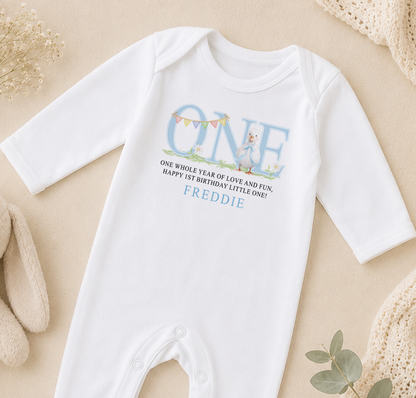 White baby onesie printed with a blue duckling, bunting and a personalised first birthday message.