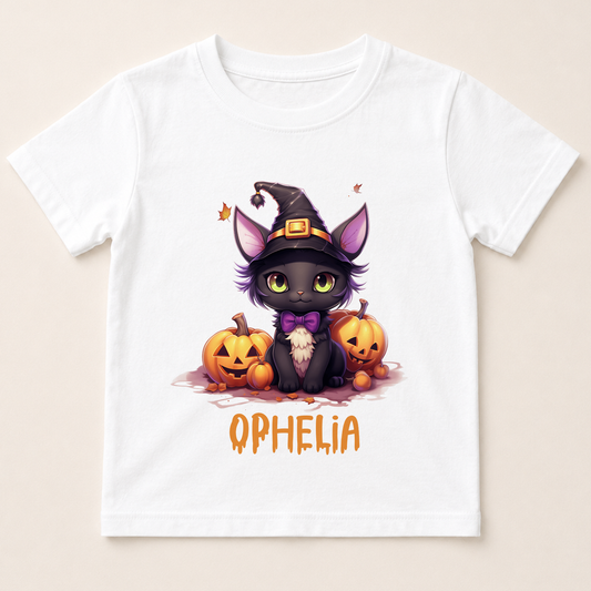 A white t-shirt with a cartoon image of a cat wearing a witch's hat and surrounded by pumpkins, with the name "QPHLIA" written below.