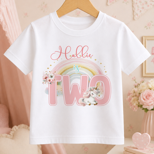 A white t-shirt with a pink unicorn and a rainbow graphic, along with the text "Hollie is two".