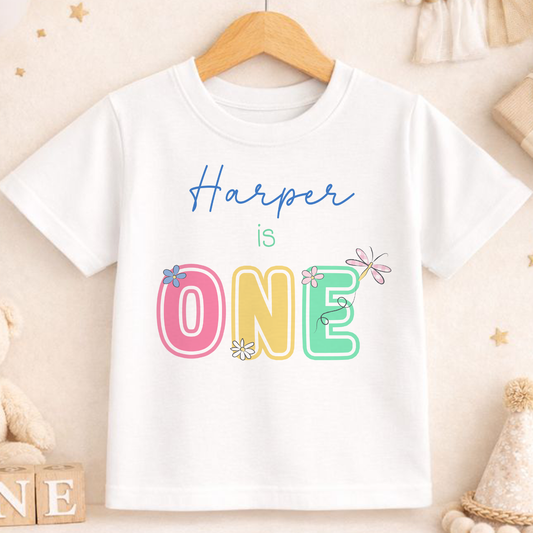 Personalised daisy and dragonfly first birthday t-shirt, printed with your child's name and 'ONE'.