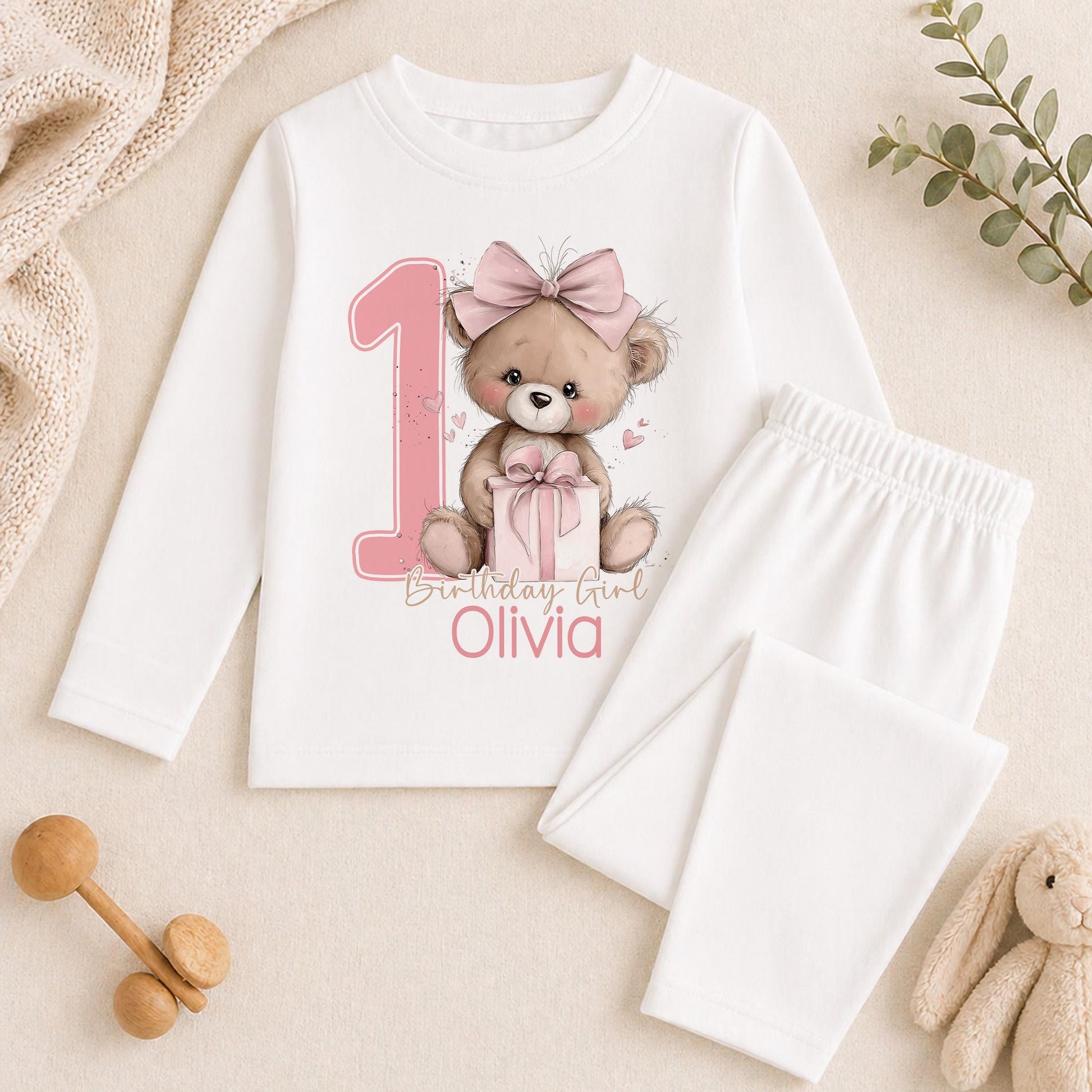 Personalised pink teddy bear first birthday outfit shown with a sample name printed on soft cotton.