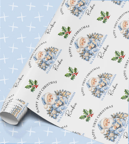 Personalised baby's first Christmas wrapping paper in pale blue with Santa in a blue suit, a frosted tree, presents and holly, relation and name