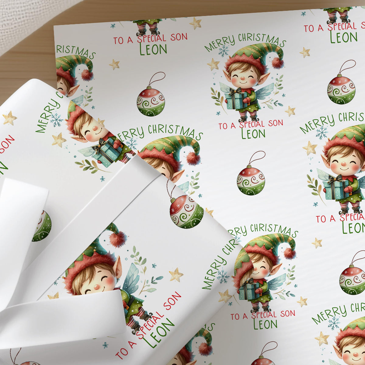 Close-up of personalised Christmas wrapping paper featuring a cute festive elf with Christmas baubles and a repeating holiday pattern on premium white gift wrap