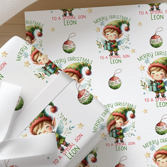 Close-up of personalised Christmas wrapping paper featuring a cute festive elf with Christmas baubles and a repeating holiday pattern on premium white gift wrap.