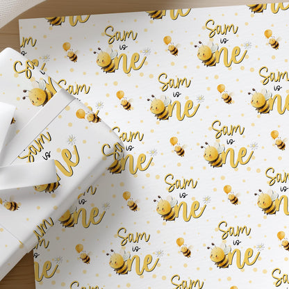 Flat lay of personalised bee 1st birthday wrapping paper with a name printed across the sheet