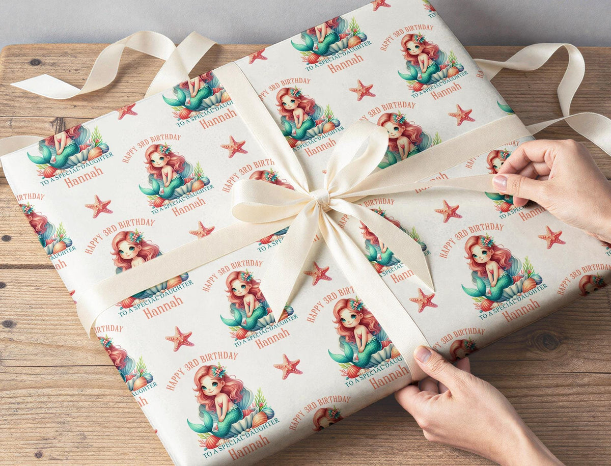 Personalised mermaid wrapping paper shown flat, displaying the repeating mermaid, seashell and starfish pattern on white paper.