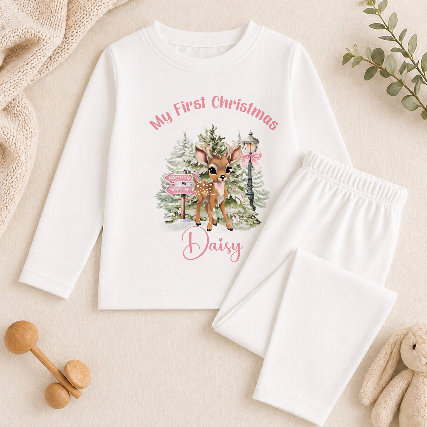 A white long-sleeved shirt with a printed image of a deer and Christmas trees, along with a pair of white pajama pants, and some stuffed animals.