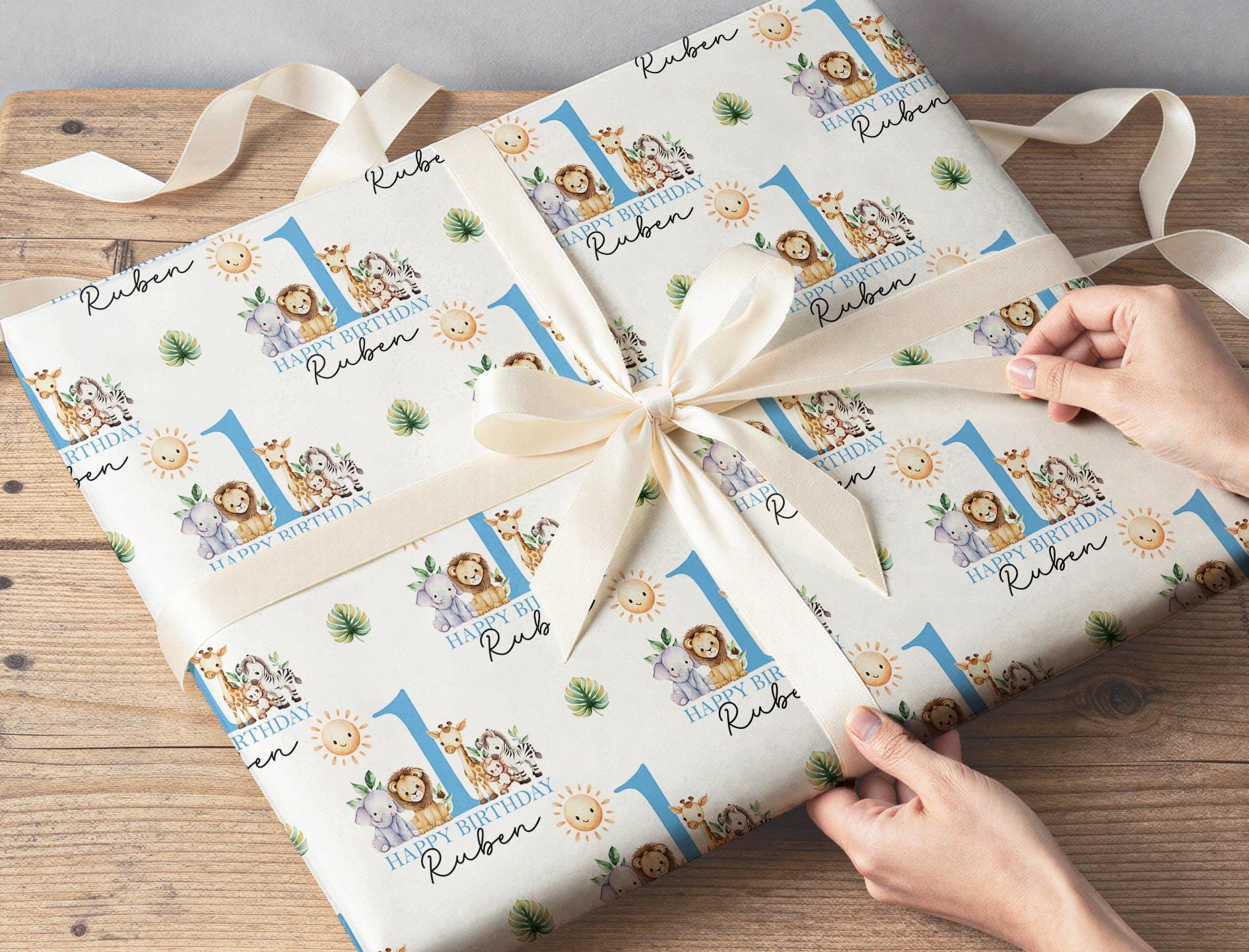 Personalised safari birthday wrapping paper with jungle animals, blue number one and custom name for boys first birthday gifts.
