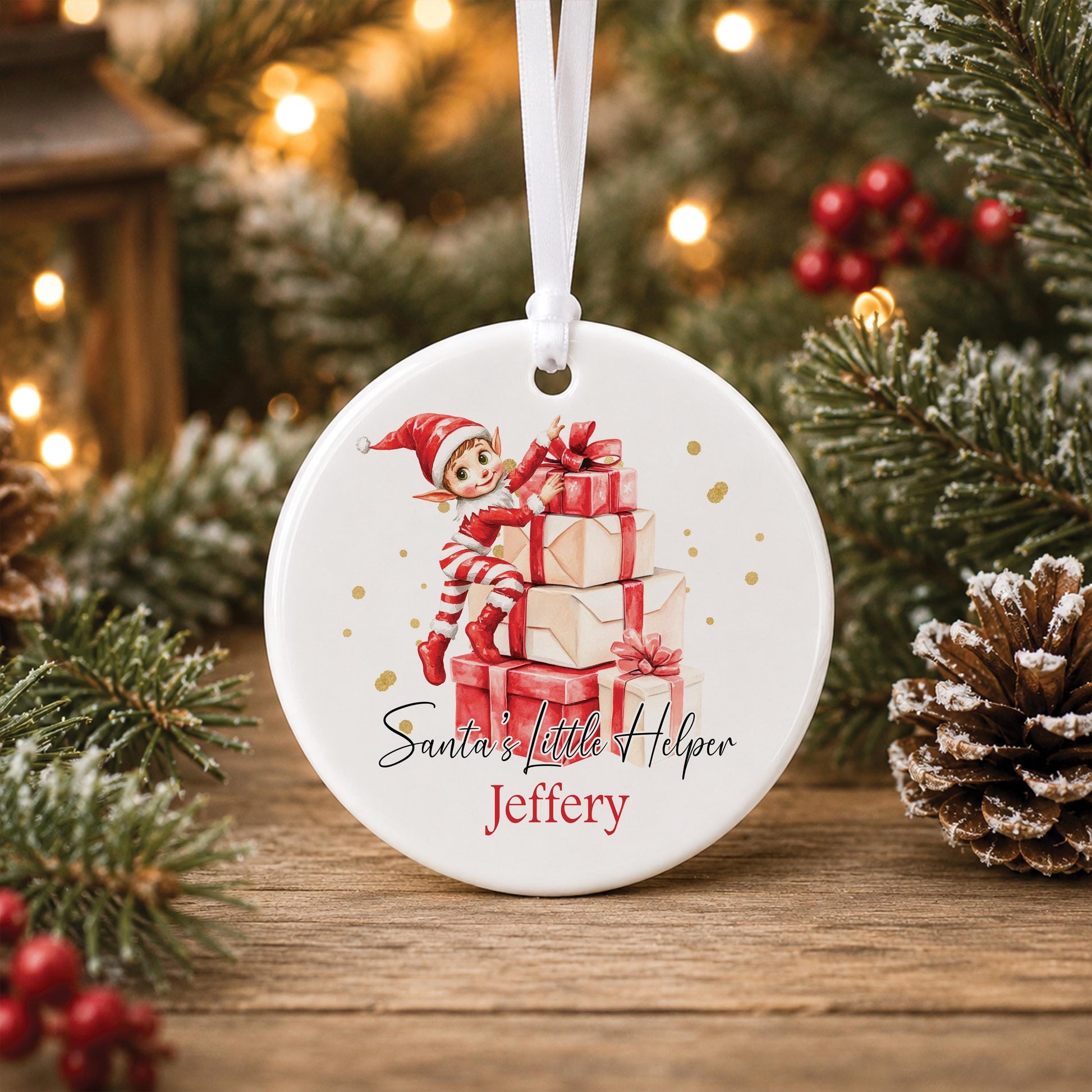 Personalised white ceramic Christmas bauble featuring a watercolour Christmas elf sitting on stacked presents, Santa’s Little Helper wording and a child’s name.