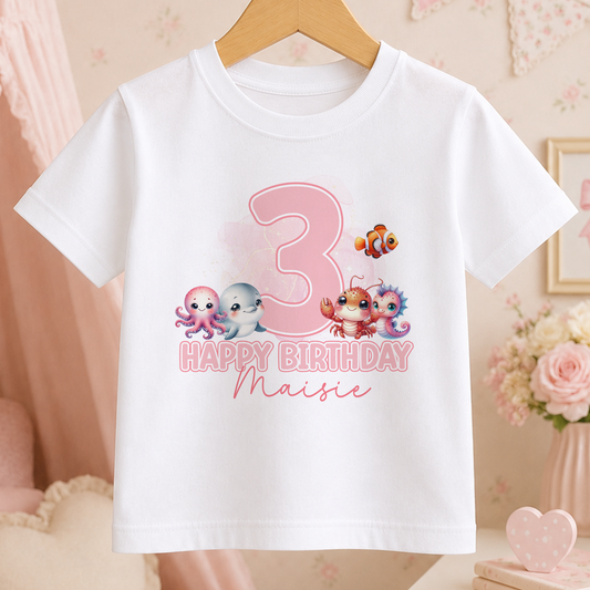 White kids t-shirt with a pink printed age number and colourful sea animal illustrations including a fish, crab and whale