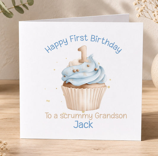 A white greeting card with a cupcake illustration and the text "Happy First Birthday To a scrummy Grandson Jack" printed on it.