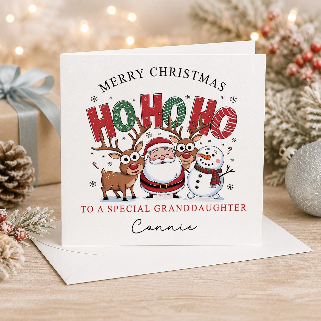 Personalised Christmas card, white 6x6 inch square card printed with HO HO HO lettering, Santa, a reindeer and a snowman with a name