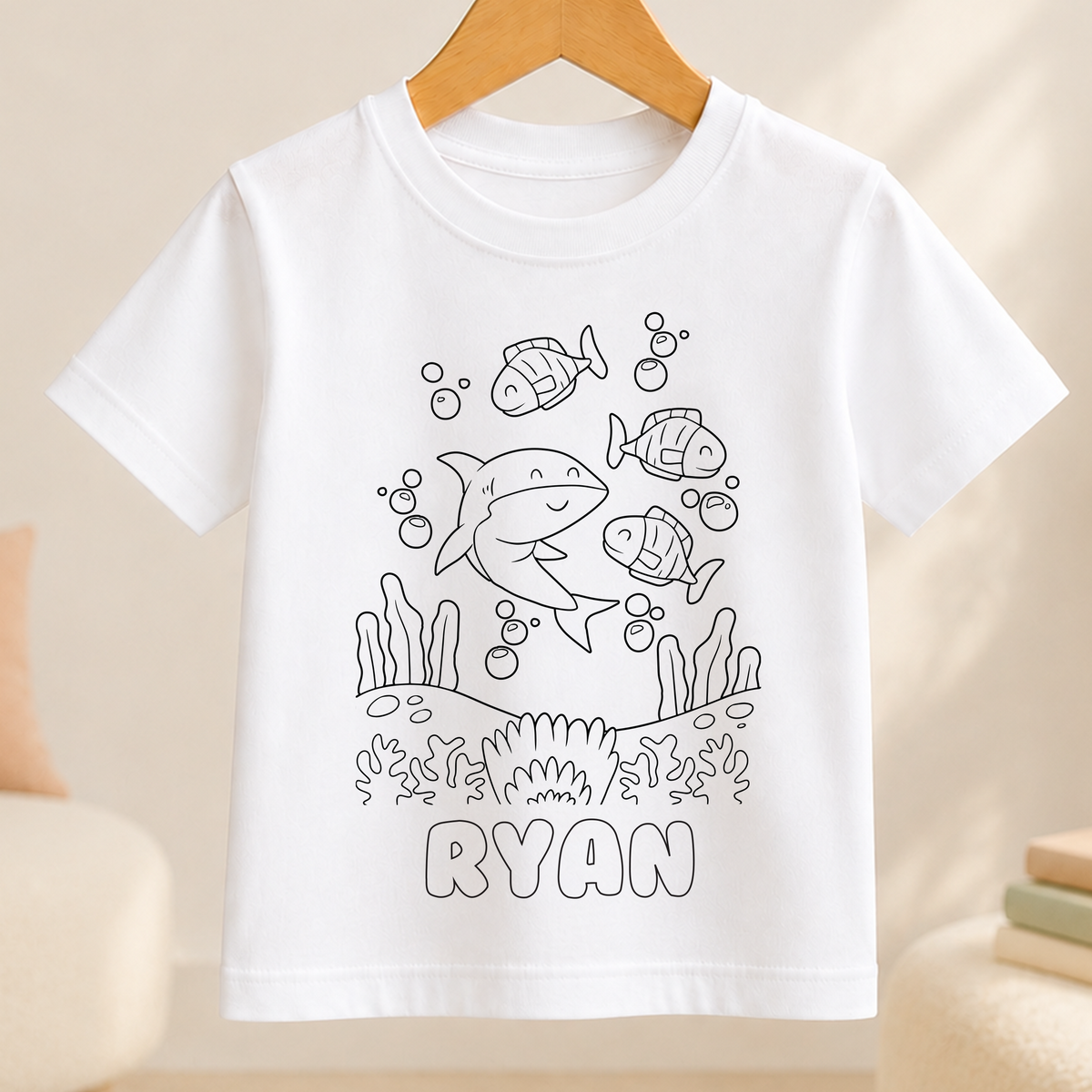 A white t-shirt with a black and white line drawing of a shark and bubbles, along with the name "RYAN" printed below.