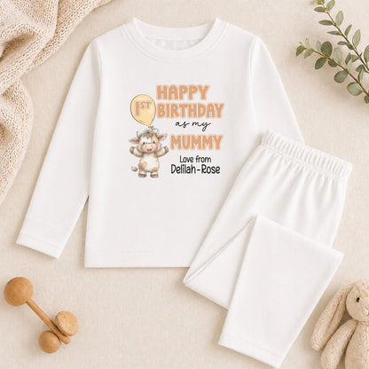 A white long-sleeved shirt with a birthday message and a cartoon image of a baby cow, along with a pair of white pants and a stuffed animal.