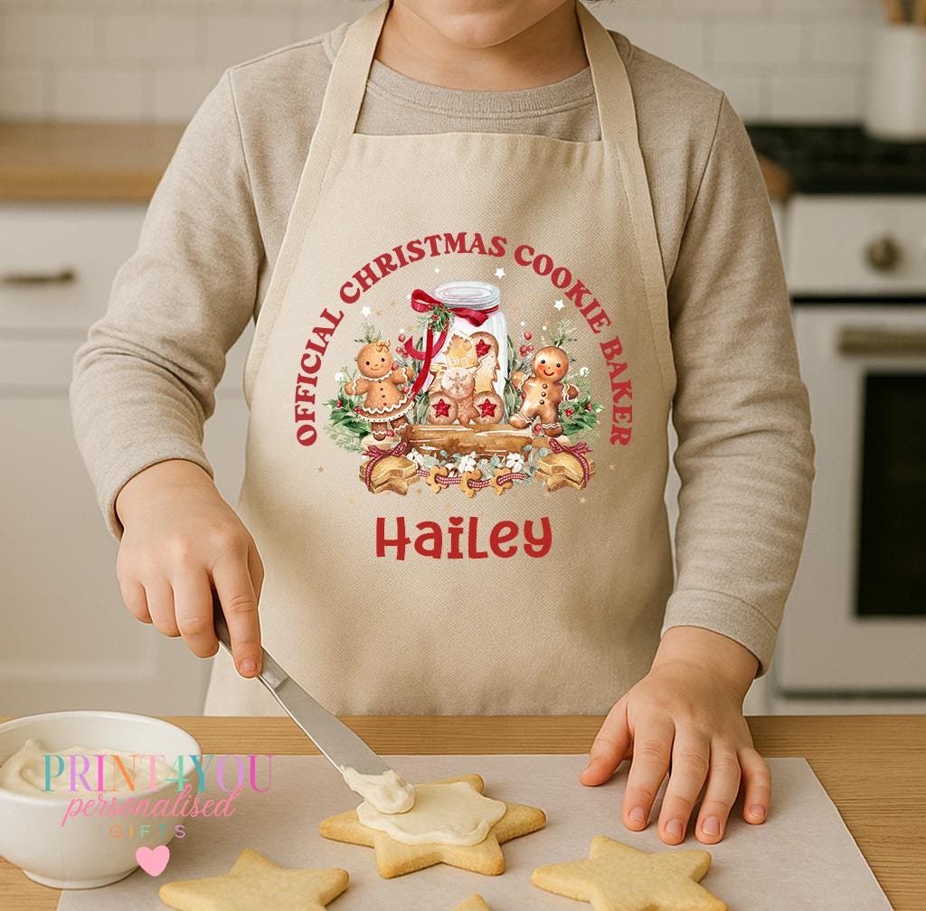 Personalised kids Christmas apron worn by a child decorating star biscuits, natural cotton apron printed with Official Christmas Cookie Baker and a name