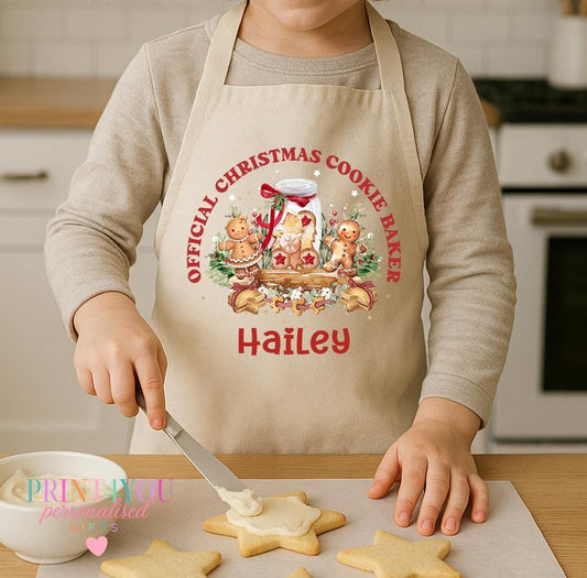 Personalised kids Christmas apron worn by a child decorating star biscuits, natural cotton apron printed with Official Christmas Cookie Baker and a name