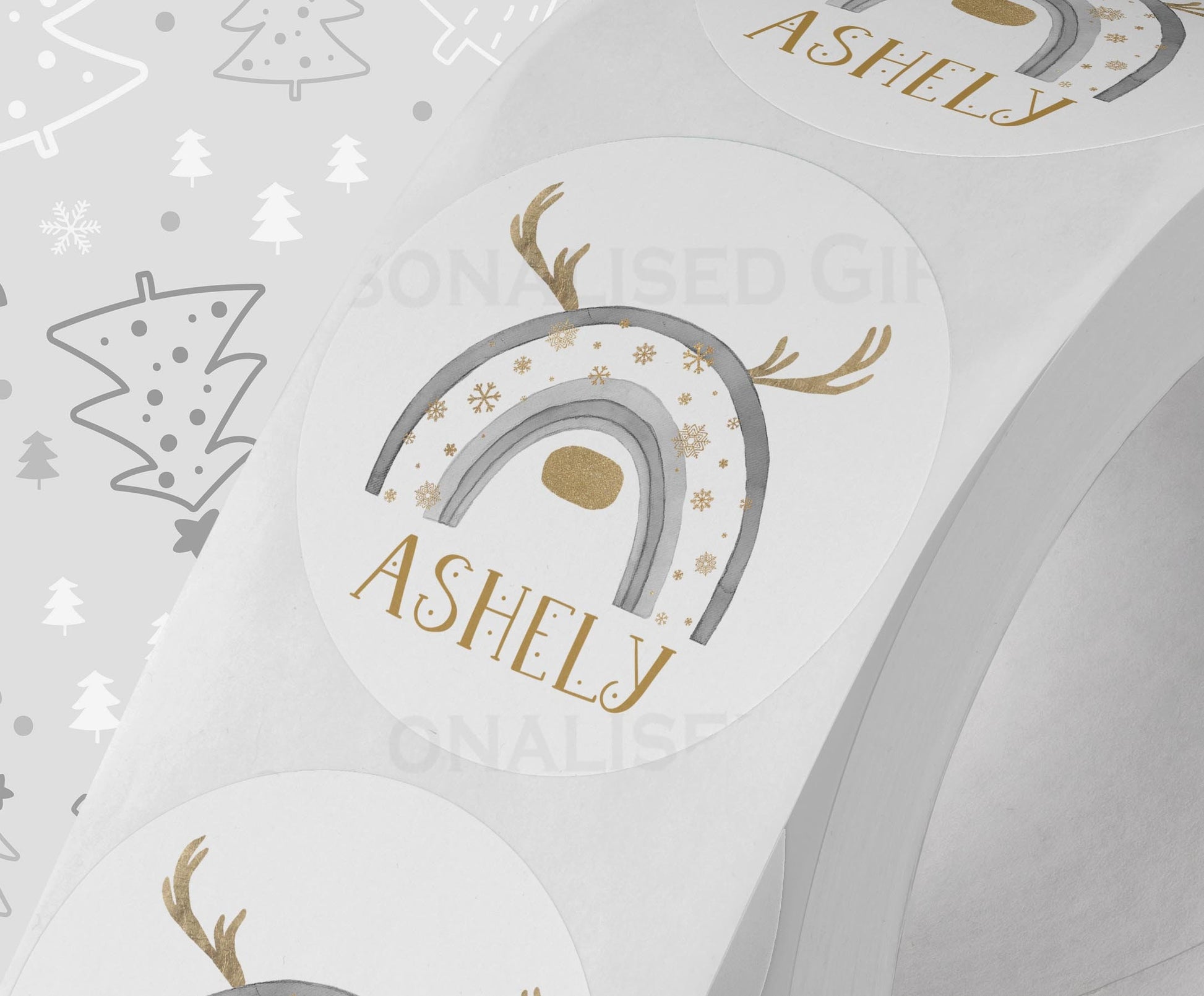 Glossy white round Christmas sticker personalised with a name, printed with a grey rainbow reindeer design, shown on a strip of stickers
