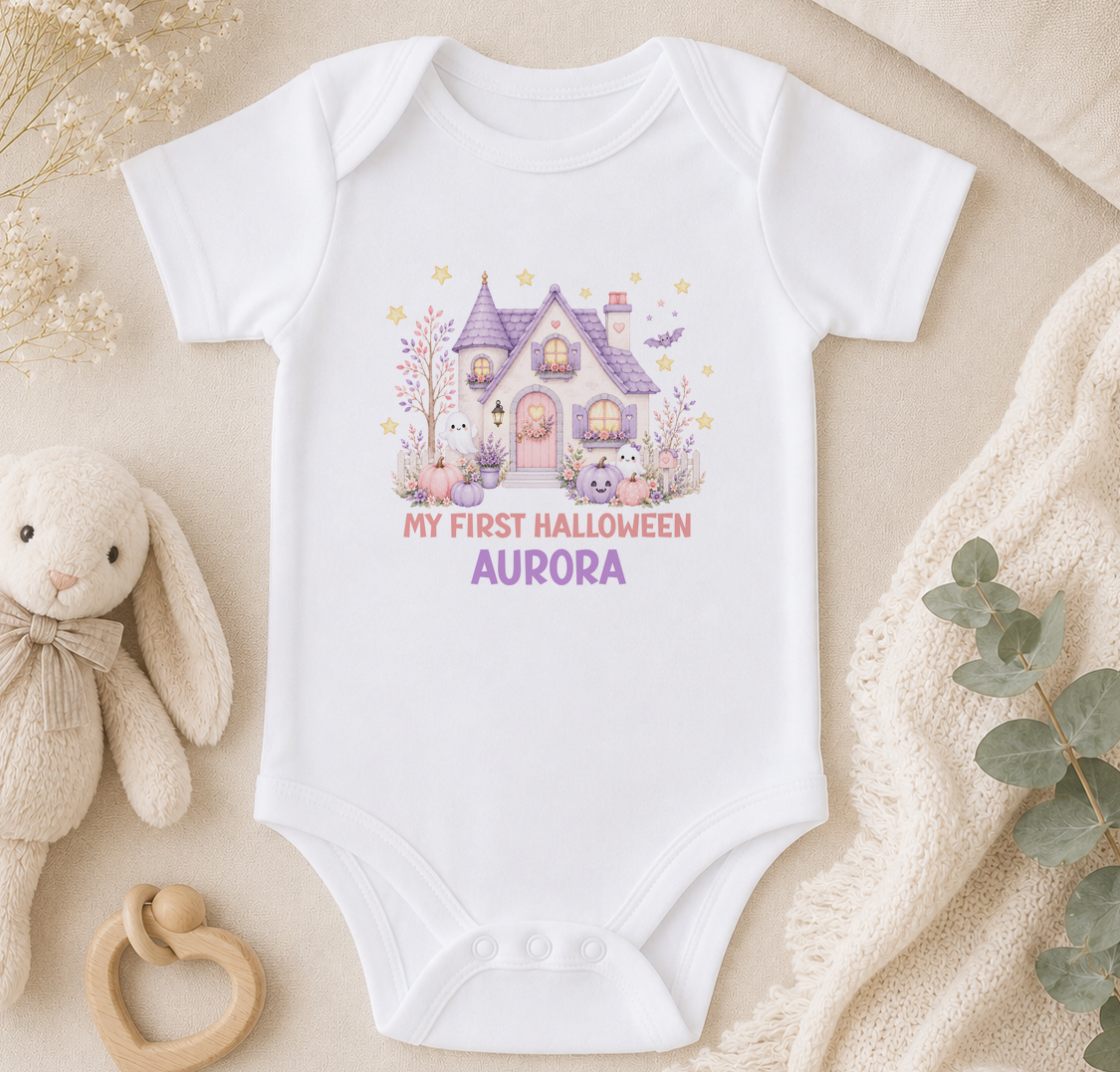 A white baby onesie with a Halloween-themed graphic, including a house, bunny, and bats, along with the text "My first Halloween Aurora".
