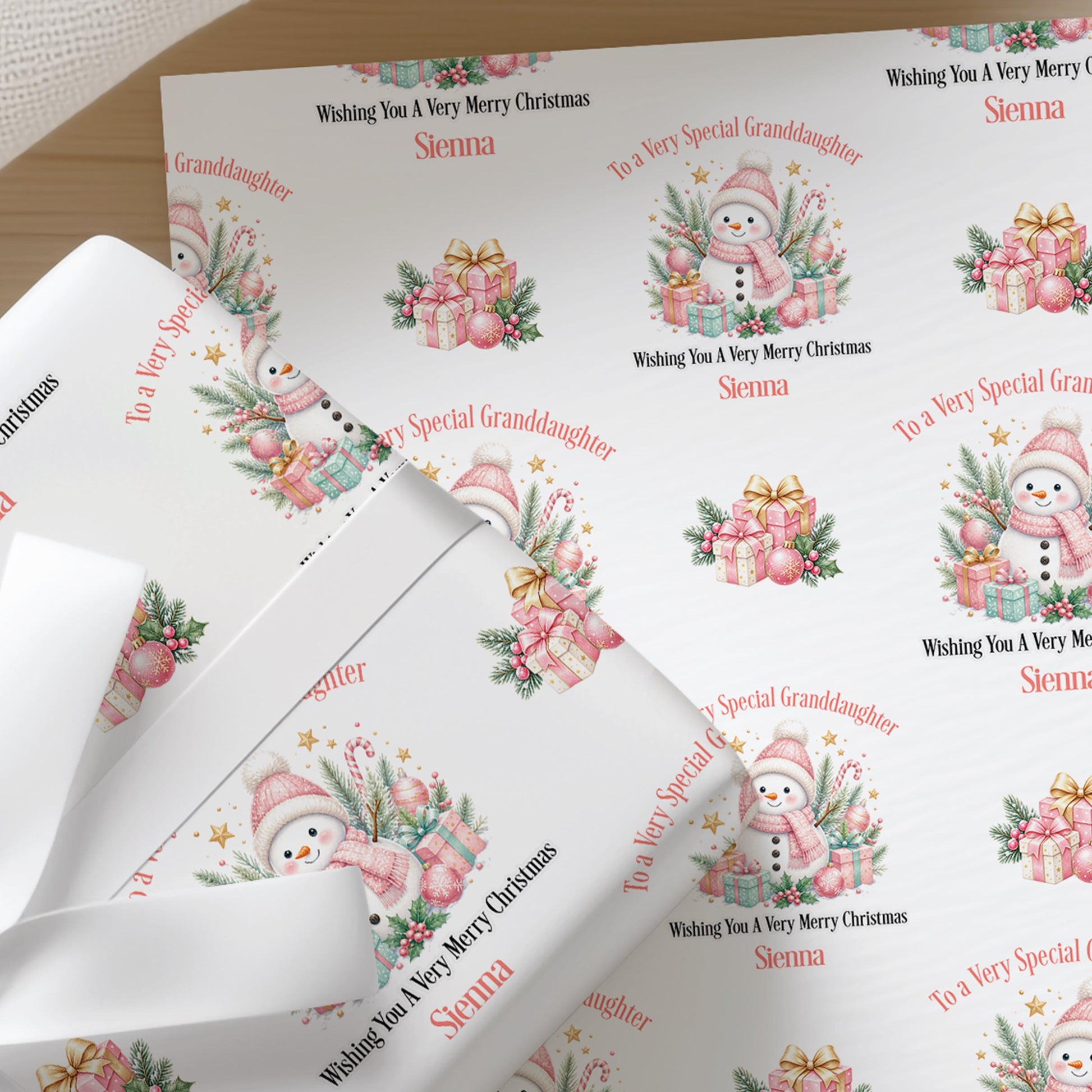 Sheets of pink snowman personalised Christmas wrapping paper folded in a gift box