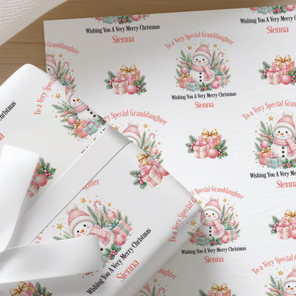 Sheets of pink snowman personalised Christmas wrapping paper folded in a gift box