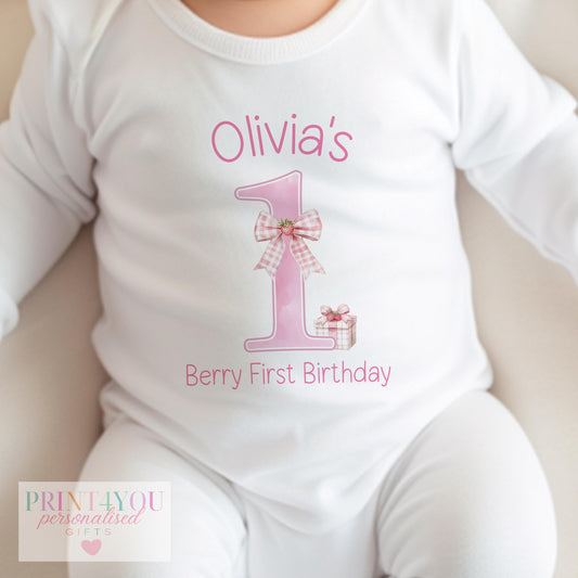 Personalised strawberry gingham first birthday outfit set laid flat on a soft cotton background.