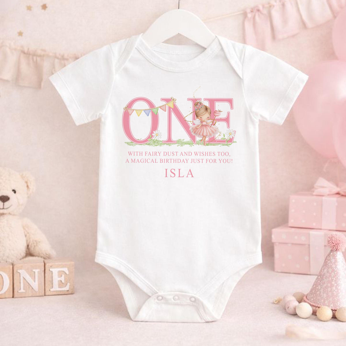 Pink first birthday garment printed with a fairy design, laid flat to show the full print.