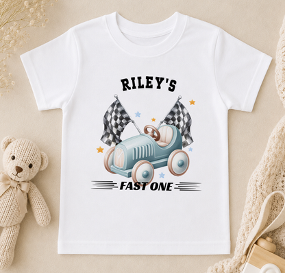 White t-shirt printed with a blue toy car, chequered flags and the text 'Riley's FAST ONE'.