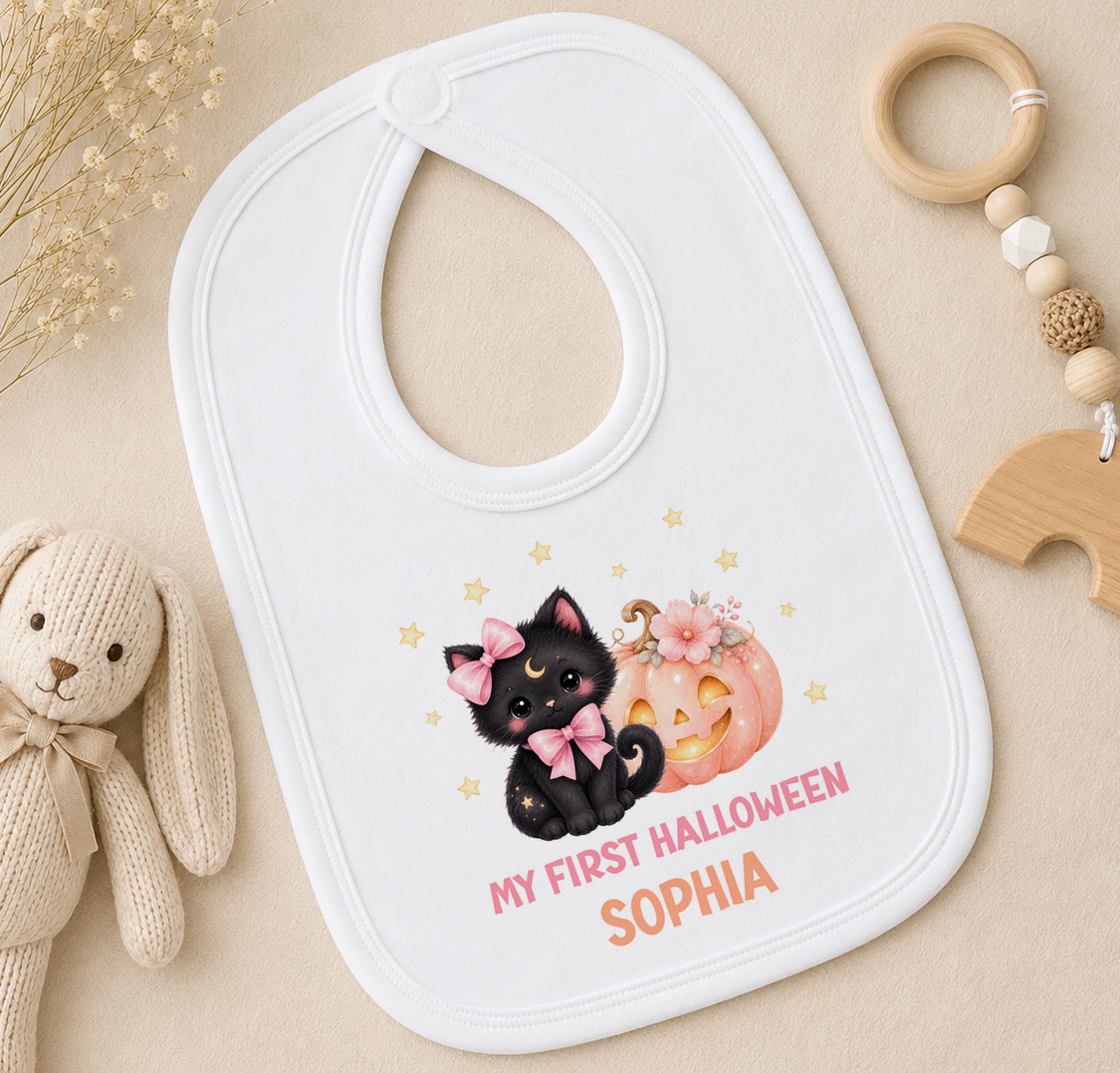 A white baby bib with a cat and pumpkin design, along with the text "My first Halloween Sophia" printed on it.