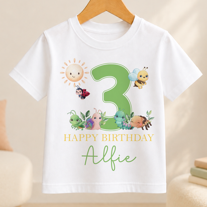 A white t-shirt with a green number 3 and various cartoon insects, including a ladybug, on it. The text below the number reads "Happy Birthday Alfie".